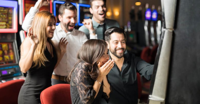 Beautiful Hispanic woman looking excited about hitting the jackpot in a slot machine while her friends celebrate with her