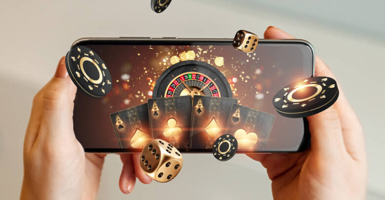 Creative background, online casino, in a man's hand a smartphone with playing cards, roulette and chips, black-gold background. Internet gambling concept. Copy space.