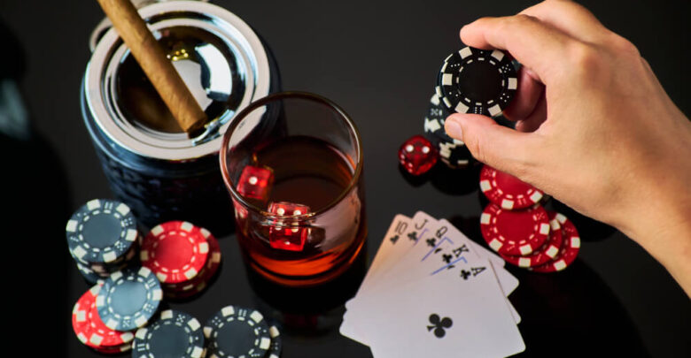 Casino chips, playing cards, glass of whiskey and dices on dark reflective background